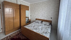 A bedroom with a wooden wardrobe, a bed with patterned bedding, a mirror, and a patterned carpet. - Charming 2-bedroom apartment in delightful Balykchy with WiFi (Balykchy)