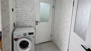 A laundry room with a white brick wall, a washing machine, and a door with a frosted glass panel. - Charming 2-bedroom apartment in delightful Balykchy with WiFi (Balykchy)