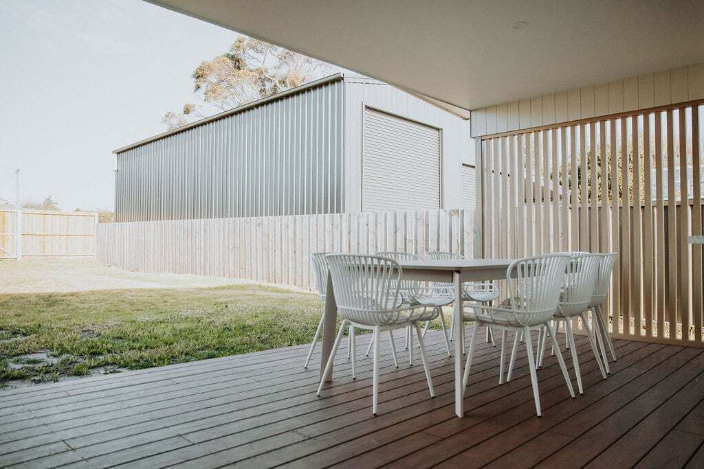 An outdoor patio with a wooden deck, white metal chairs, and a table.