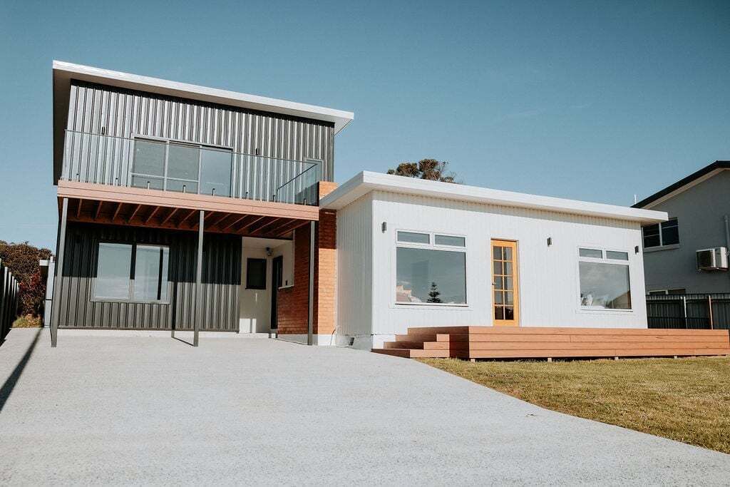 Een modern huis met twee verdiepingen, een plat dak, grote ramen en een houten terras.