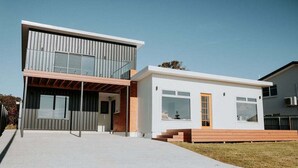 A modern two-story house with a flat roof, large windows, and a wooden deck. - Bichenobae, where coastal cool meets comfort and fun (Bicheno)
