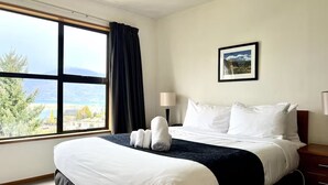 Ein Hotelzimmer mit einem großen Bett, einem Fenster mit Ausblick, einem gerahmten Bild an der Wand und einem Nachttisch mit Lampe.