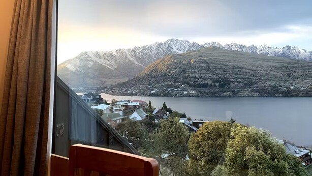 Ein Zimmer mit großem Fenster mit Blick auf einen See und schneebedeckte Berge.