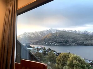 Ein Zimmer mit großem Fenster mit Blick auf einen See und schneebedeckte Berge.