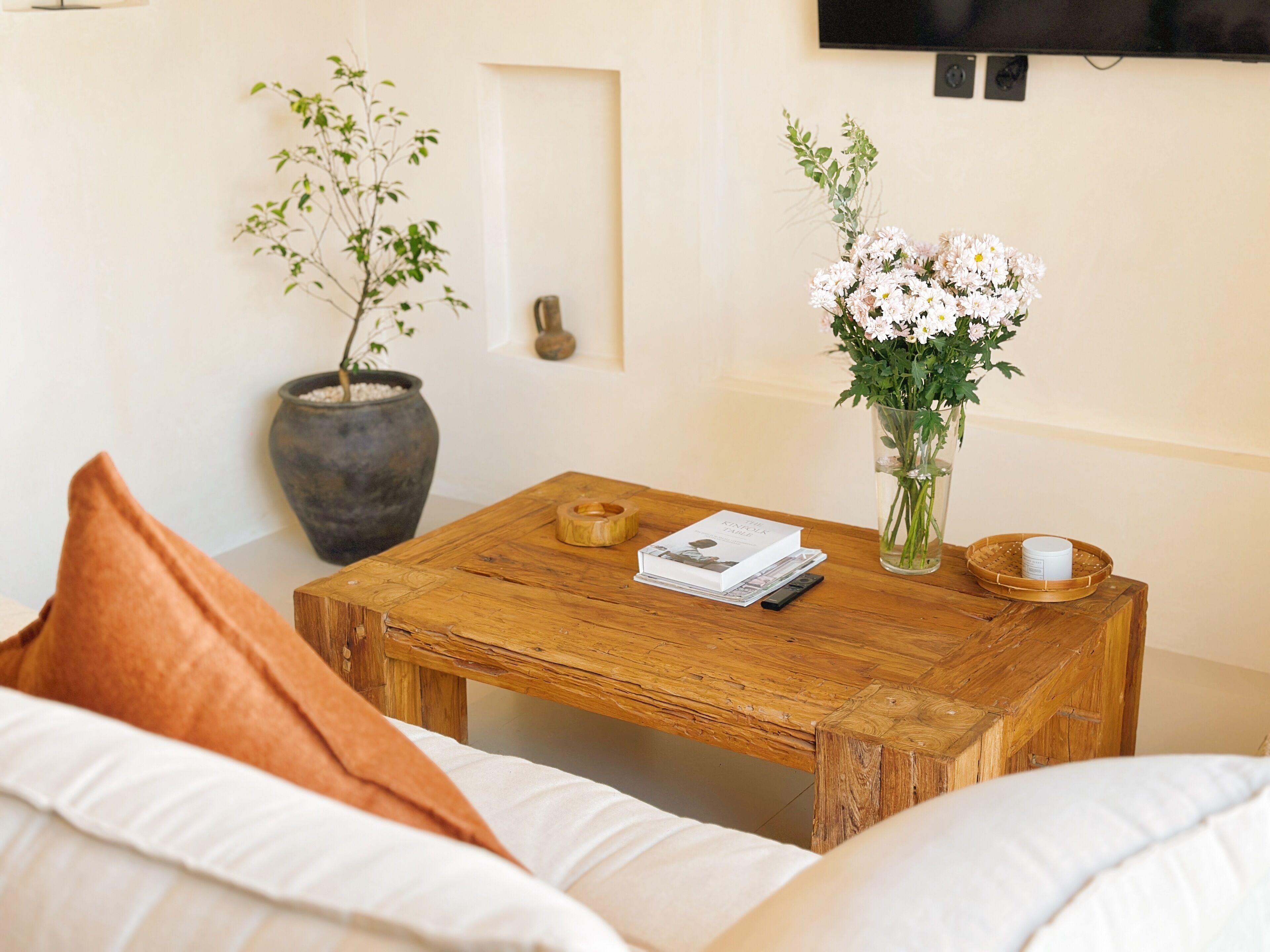 Un salon chaleureux avec une table basse en bois, une plante en pot, un vase rempli de fleurs et un livre.