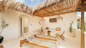 A sunlit outdoor lounge area with a thatched roof, wicker furniture, and a small table with a plant. - Casa Mahina Umalas (Kerobokan)