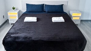 Ein modernes Schlafzimmer mit einem großen Bett, zwei Kissen, einem Nachttisch mit Lampe und einem Bild an der Wand.