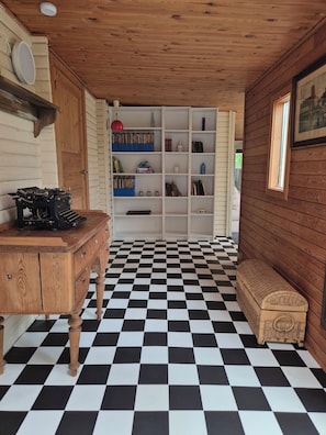 Ein Zimmer mit Schachbrettmuster auf dem Boden, einem Holztisch, einem BĂŒcherregal und einer Korbsitzbank.