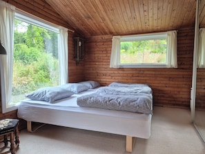 Ein Zimmer in einer HolzhĂŒtte mit einem Bett, einer Uhr und einem Fenster mit VorhĂ€ngen.