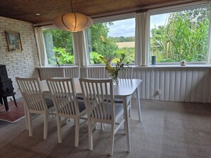 Ein Zimmer mit Tisch, Stühlen, einer Pendelleuchte, einem fenster mit Vorhängen und einer Heizung.