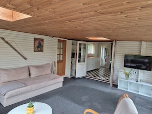 Ein gemütliches Zimmer mit Holzboden, einer Couch, einem Fernseher und einem kleinen Tisch mit einer Pflanze.