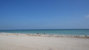 Une plage de sable fin, sous un ciel bleu clair et une mer calme.