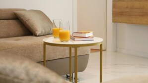 Un soggiorno moderno con un divano color beige, un tavolino rotondo con un libro e bicchieri di succo d'arancia, e una casa in miniatura su uno scaffale.