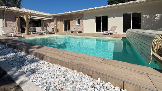 A swimming pool with lounge chairs and a pergola, surrounded by a stone wall and a wooden deck.