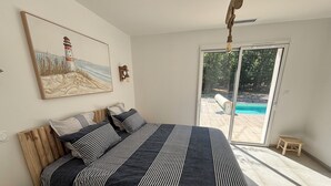 A bedroom with a large bed, a painting of a lighthouse, a wooden headboard, and a view of a pool through a sliding glass door.