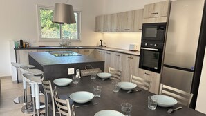 A modern kitchen with a central island, bar stools, and a dining table set for six.