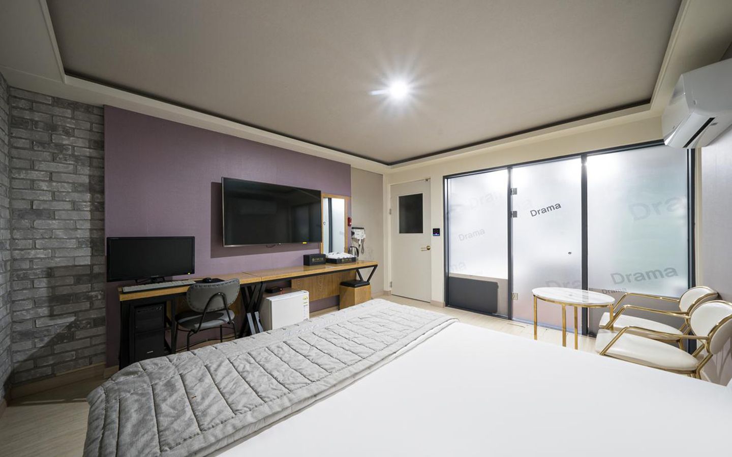 A modern hotel room with a large bed, a desk with a computer, a TV, and a seating area with chairs.