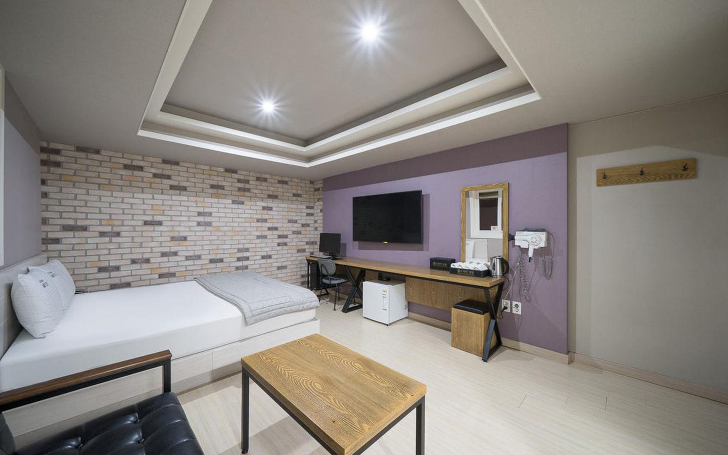 Una habitación moderna con pared de ladrillo, un sofá blanco, un escritorio de madera, una computadora y un televisor.