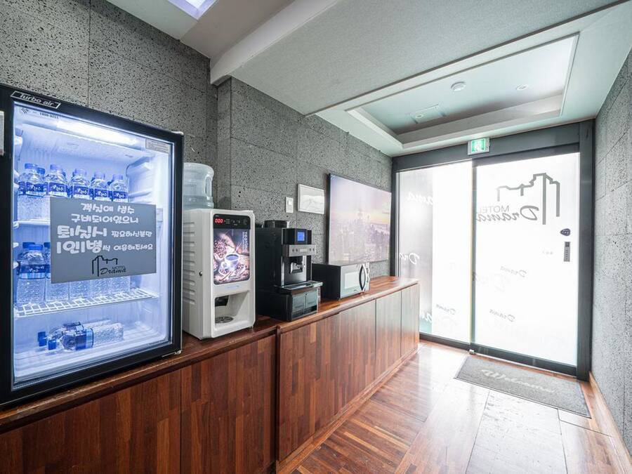 Zona de recepción con pantalla digital mostrando un anuncio de bebidas, una máquina de café y un dispensador de agua.