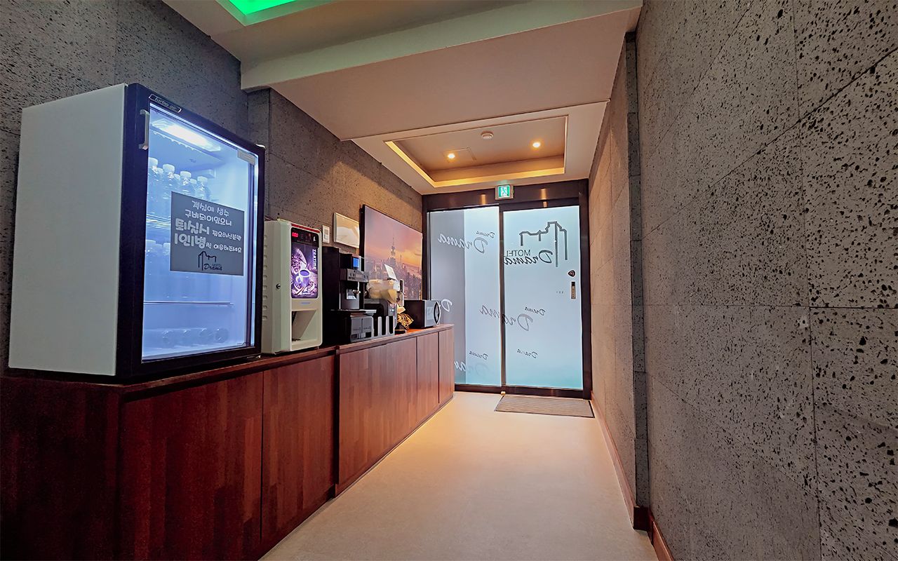 Una zona de recepción con un mostrador de madera, una pantalla digital y una puerta de cristal con diseño de paisaje urbano.