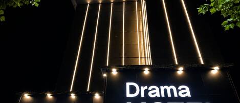 A building with illuminated signs reading 'Drama MOTEL' and a tree in the foreground.