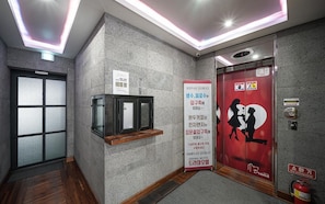 An elevator interior with a fire extinguisher, a sign with Korean text, and a silhouette of a woman on the door. - Daegu Suseong DRAMA (Daegu)