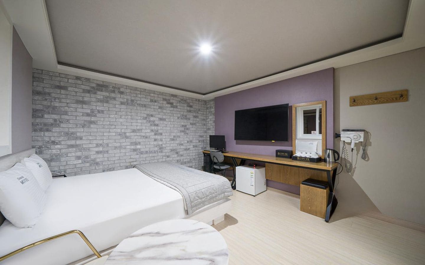 Una habitación de hotel con cama, escritorio, computadora y pared de ladrillo.