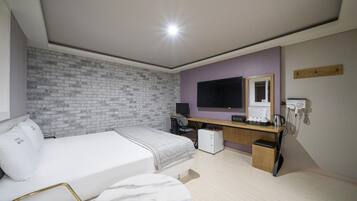 Una habitación de hotel con cama, escritorio, computadora y pared de ladrillo.