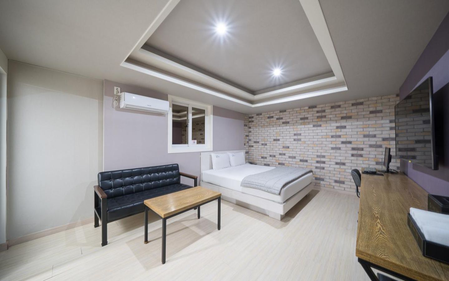 Un dormitorio moderno con cama, sofá, una mesita y televisor.