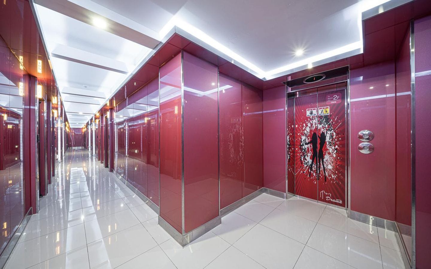 A modern hallway with glass doors and a red wall, leading to an elevator.