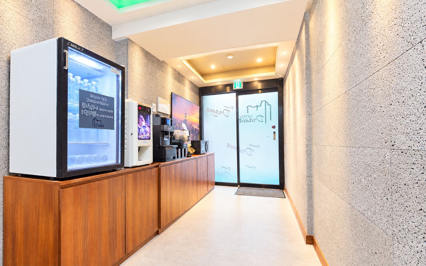Zona de recepció amb mostrador de fusta, pantalla digital i porta de vidre que dóna a un vestíbul.