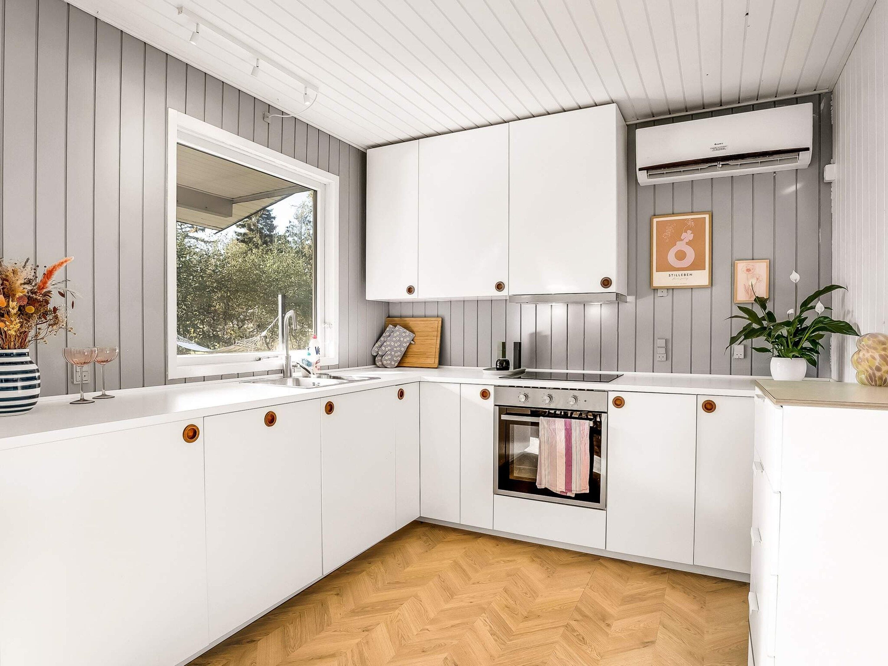 Une cuisine moderne avec des meubles blancs, un four encastré et une fenêtre qui laisse entrer la lumière naturelle.