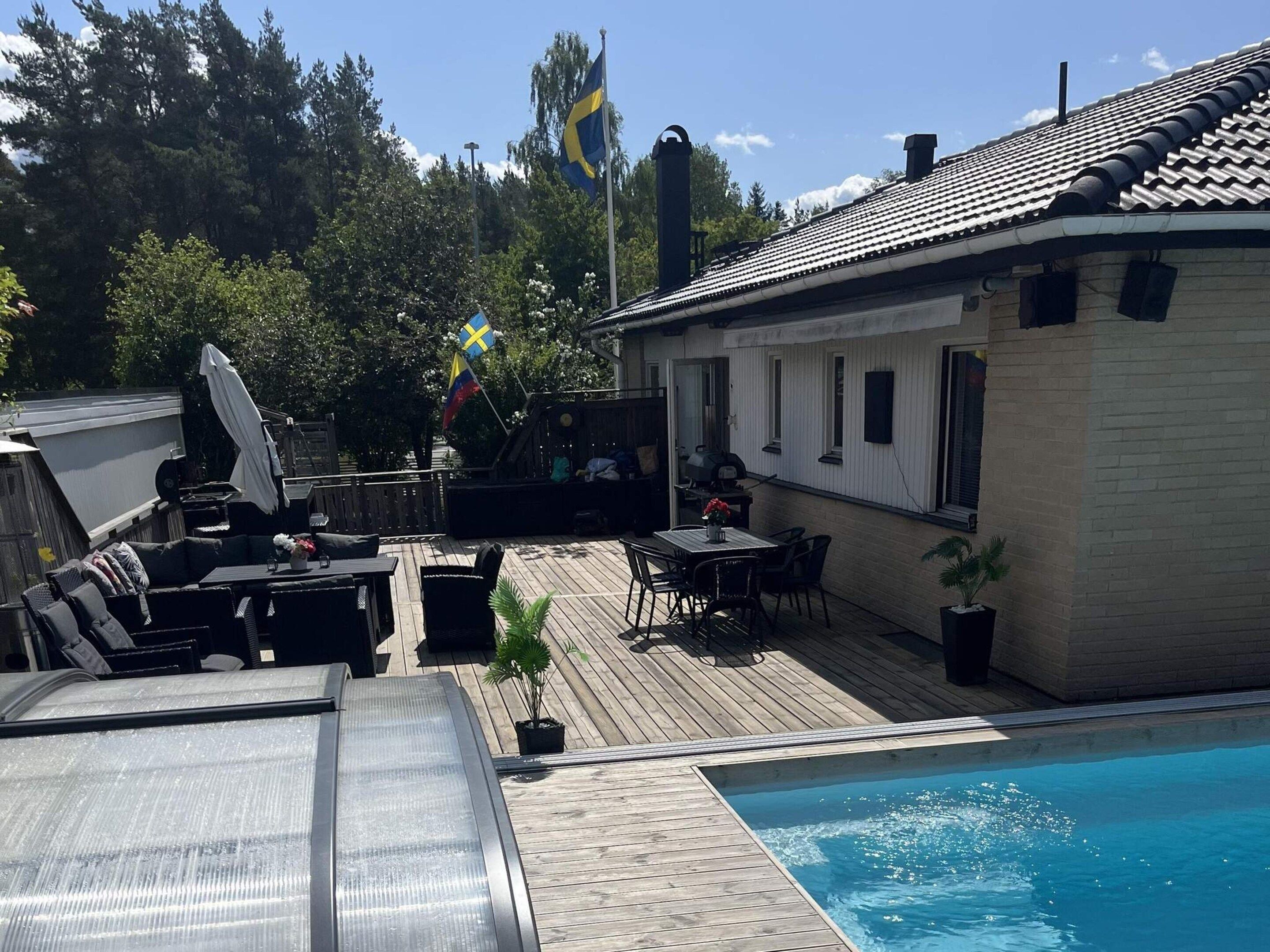 A poolside area with a wooden deck, lounge chairs, a barbecue grill, and a small table with chairs.
