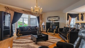 A spacious living room with a chandelier, black sofas with gold trim, a coffee table, and a large mirror on the wall.