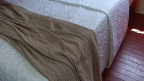 Un lit avec une literie blanche et un plaid marron, un plancher en bois et une fenêtre à carreaux.