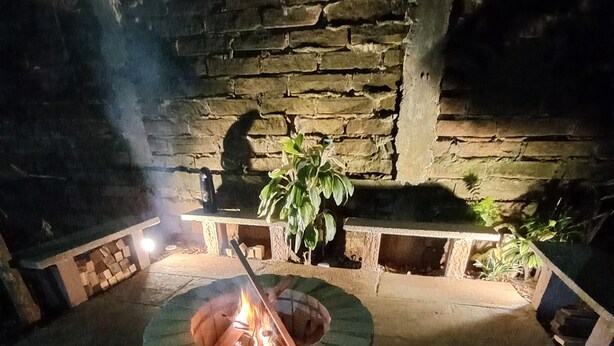 Un muret en pierre avec un foyer circulaire au centre, entouré d’espaces pour s’asseoir et de plantes en pot.