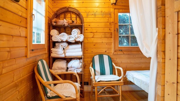 Una habitación de cabaña acogedora con paredes de madera, una cama, dos sillas de mimbre y un estante con toallas dobladas cuidadosamente.