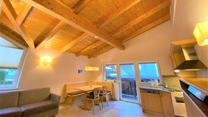 Una cocina acogedora con vigas de madera, un comedor con banco y vistas a través de amplios ventanales.