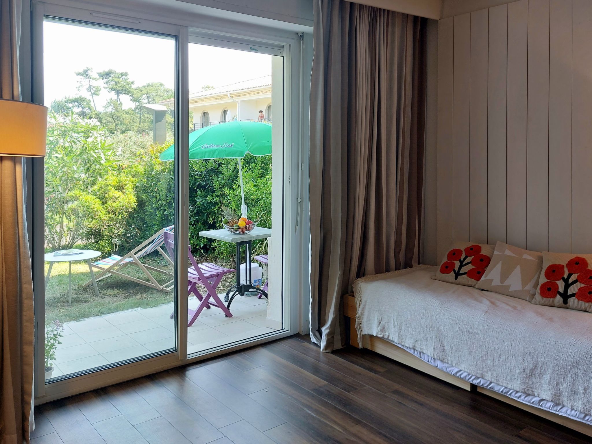 A room with a bed, a table with a green umbrella, and a view of the outdoors.