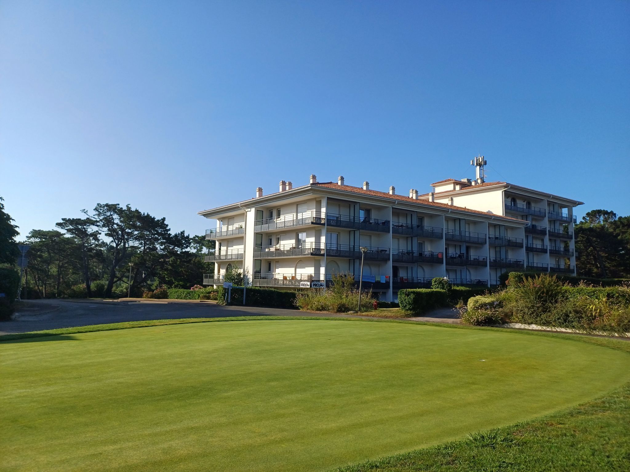 A multi-story building with balconies, surrounded by well-maintained lawns and trees.