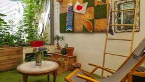 Un petit espace jardin aménagé avec une chaise en bois, une table ronde ornée d’un vase de fleurs et diverses plantes en pot.