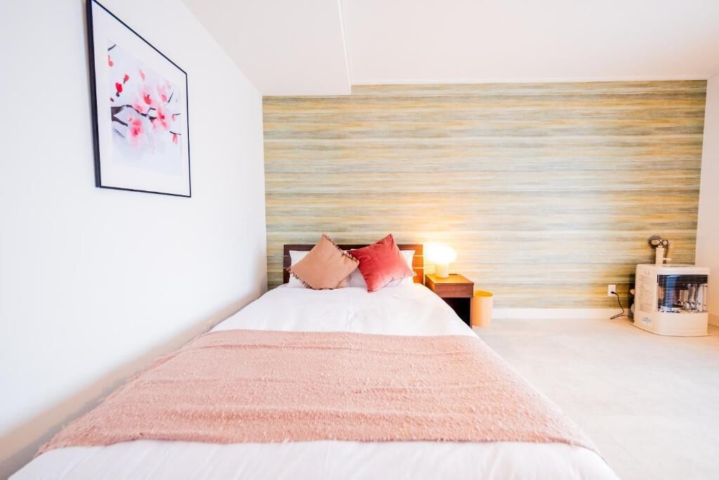 Ein ordentlich eingerichtetes Schlafzimmer mit Bett, Kissen, Nachttisch mit Lampe und einer Wand-Klimaanlage.