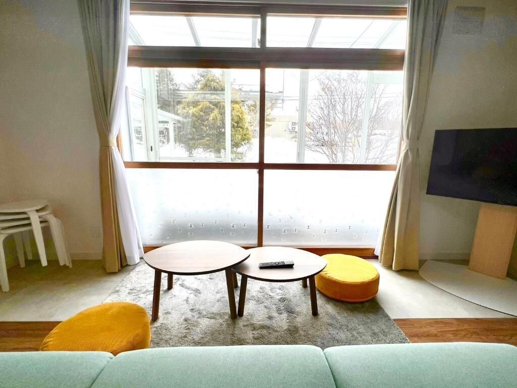 Un salon avec une grande fenêtre, deux tables rondes, un canapé et un téléviseur.