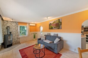 A living room with a stone wall, a gray sofa, a red rug, a small table with a candle, and a fireplace. - Holiday Home 'Ferienhaus Am Rander Der Lewitz' with Lake View, Wi-Fi and Air Conditioning (Lewitzrand)