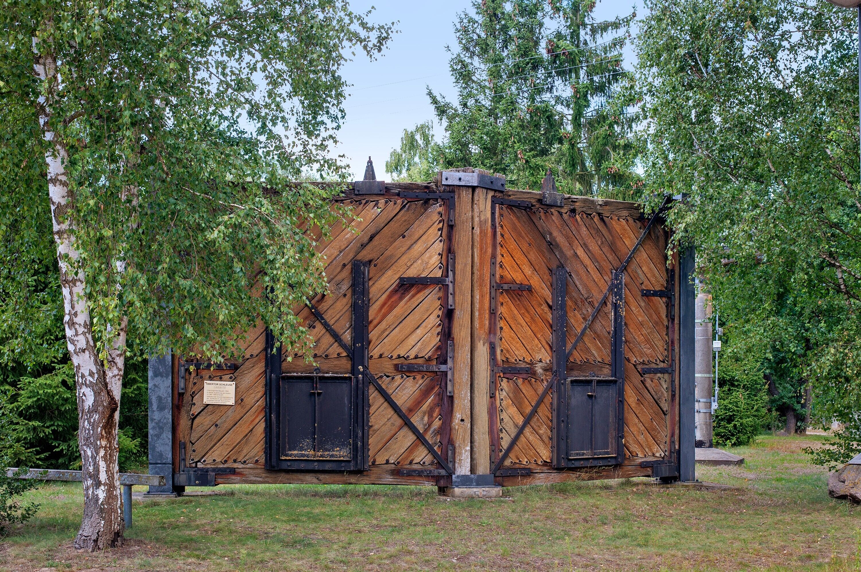 Une structure rustique en bois, renforcée par des éléments métalliques, et entourée d’arbres.