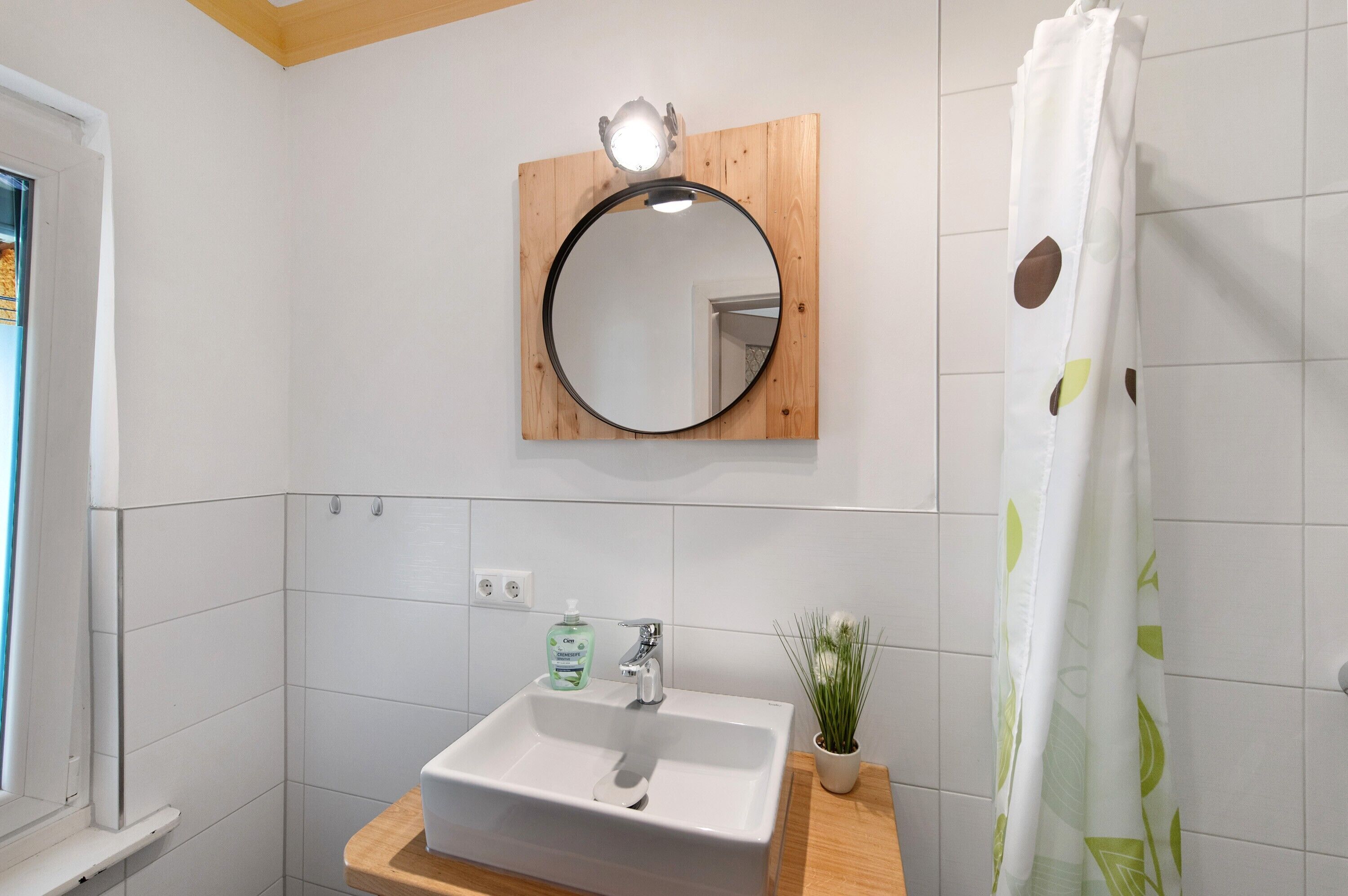 A bathroom with a white sink, a mirror, a shower curtain, and a small potted plant.