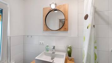A bathroom with a white sink, a mirror, a shower curtain, and a small potted plant.