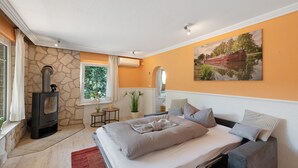 A bedroom with a stone wall, a bed with grey bedding, a small table with a plant, and a painting of a boat on the wall. - Holiday Home 'Ferienhaus Am Rander Der Lewitz' with Lake View, Wi-Fi and Air Conditioning (Lewitzrand)