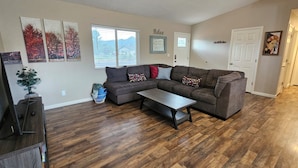 A living room with a sectional sofa, a coffee table, hardwood flooring, a potted plant, and artwork on the walls.