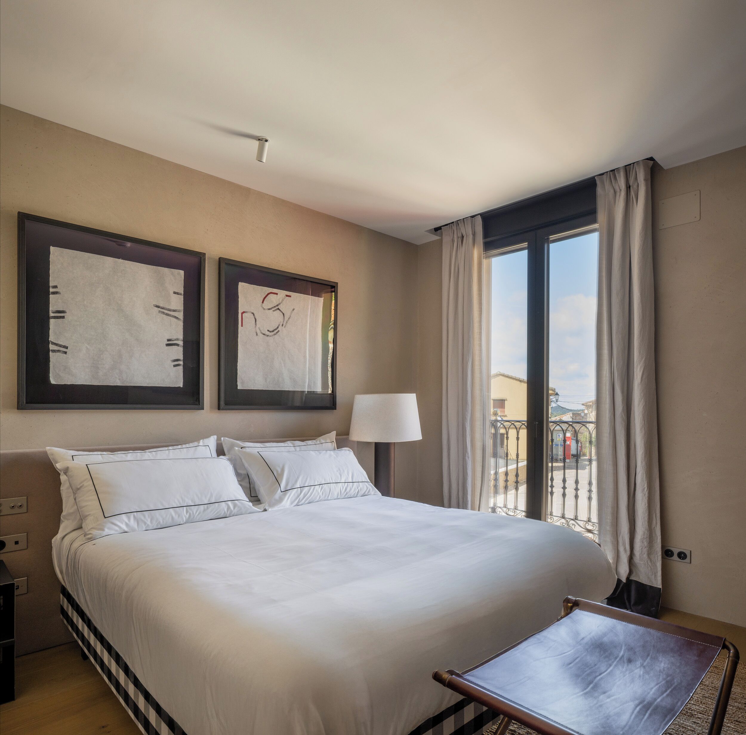 Habitación de hotel con una cama grande, una mesita de noche, una lámpara y vistas al exterior a través de una ventana.